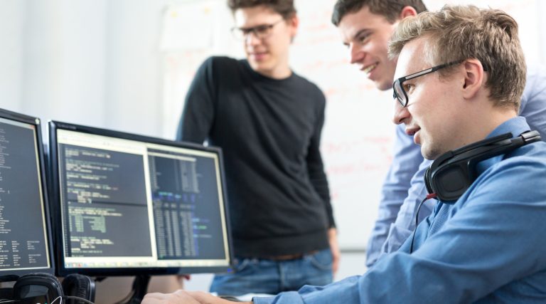 Tři mladi programátoři se dívají do monitorů