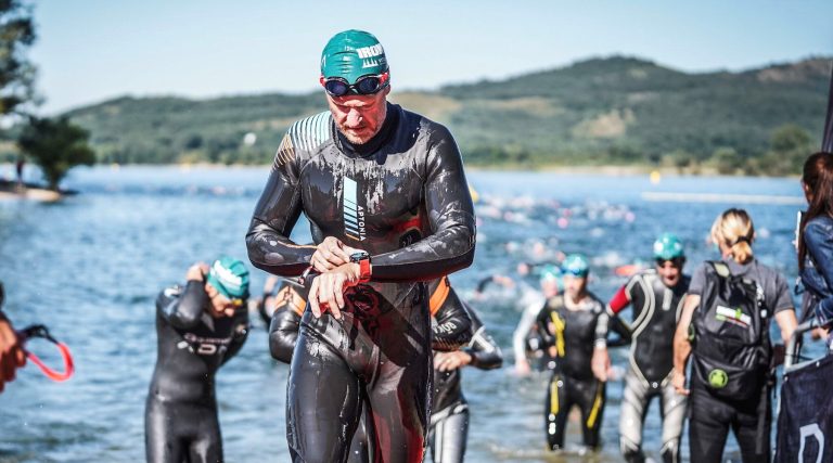 Petr vyléza v neoprenu z vody, sleduje sportovní hodinky